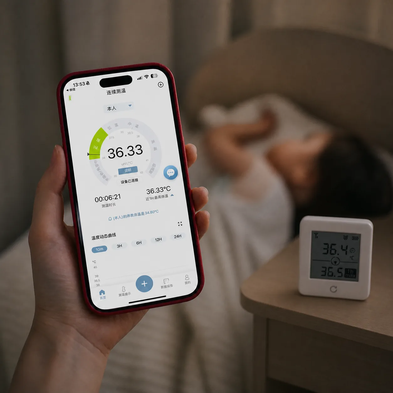 OnCorva bedside temperature monitor on a side table while a caregiver follows the same continuous body temperature reading in the phone app
