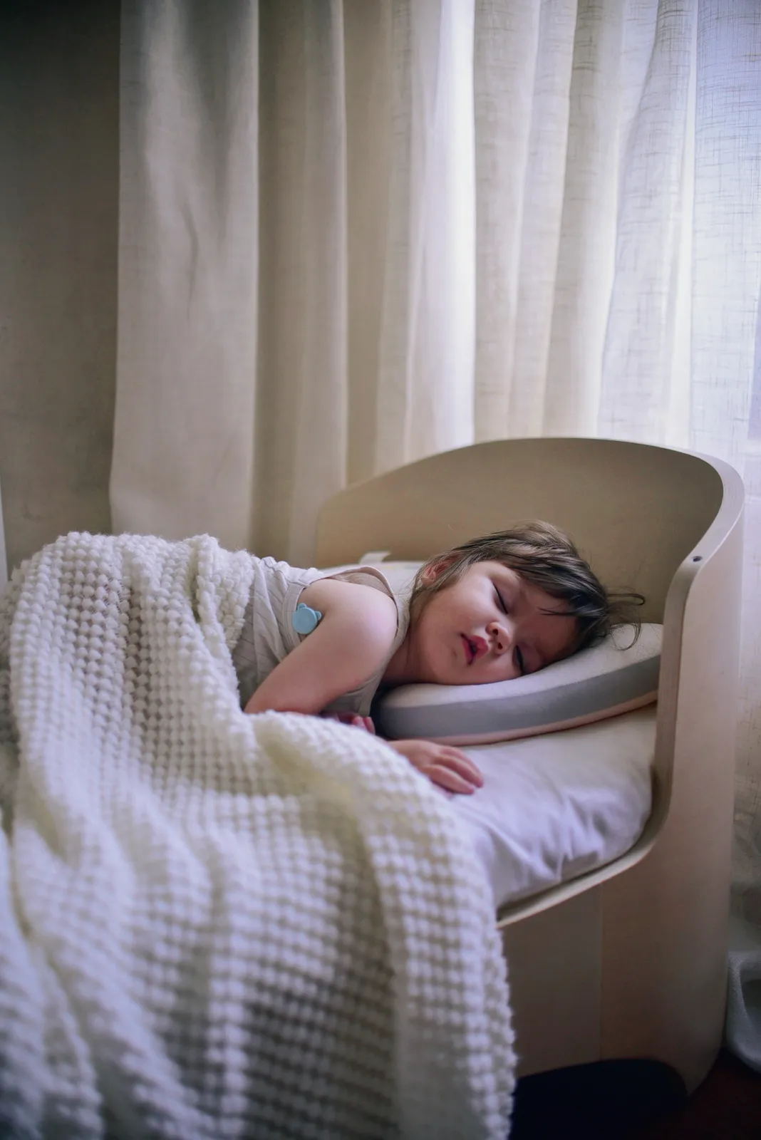 Child asleep in a crib wearing the OnCorva fever monitor