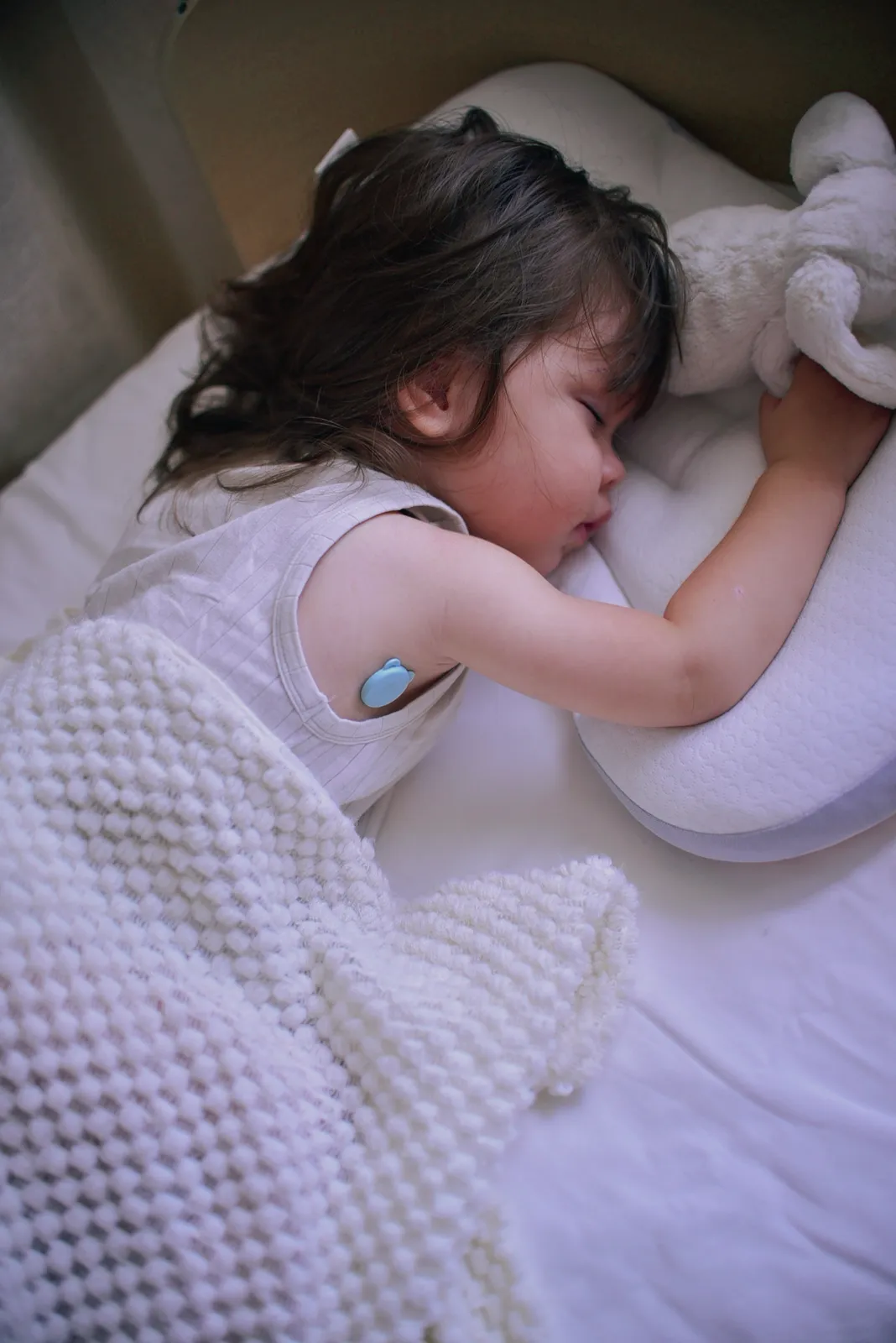 Child asleep at home wearing a OnCorva continuous temperature monitor on the upper arm