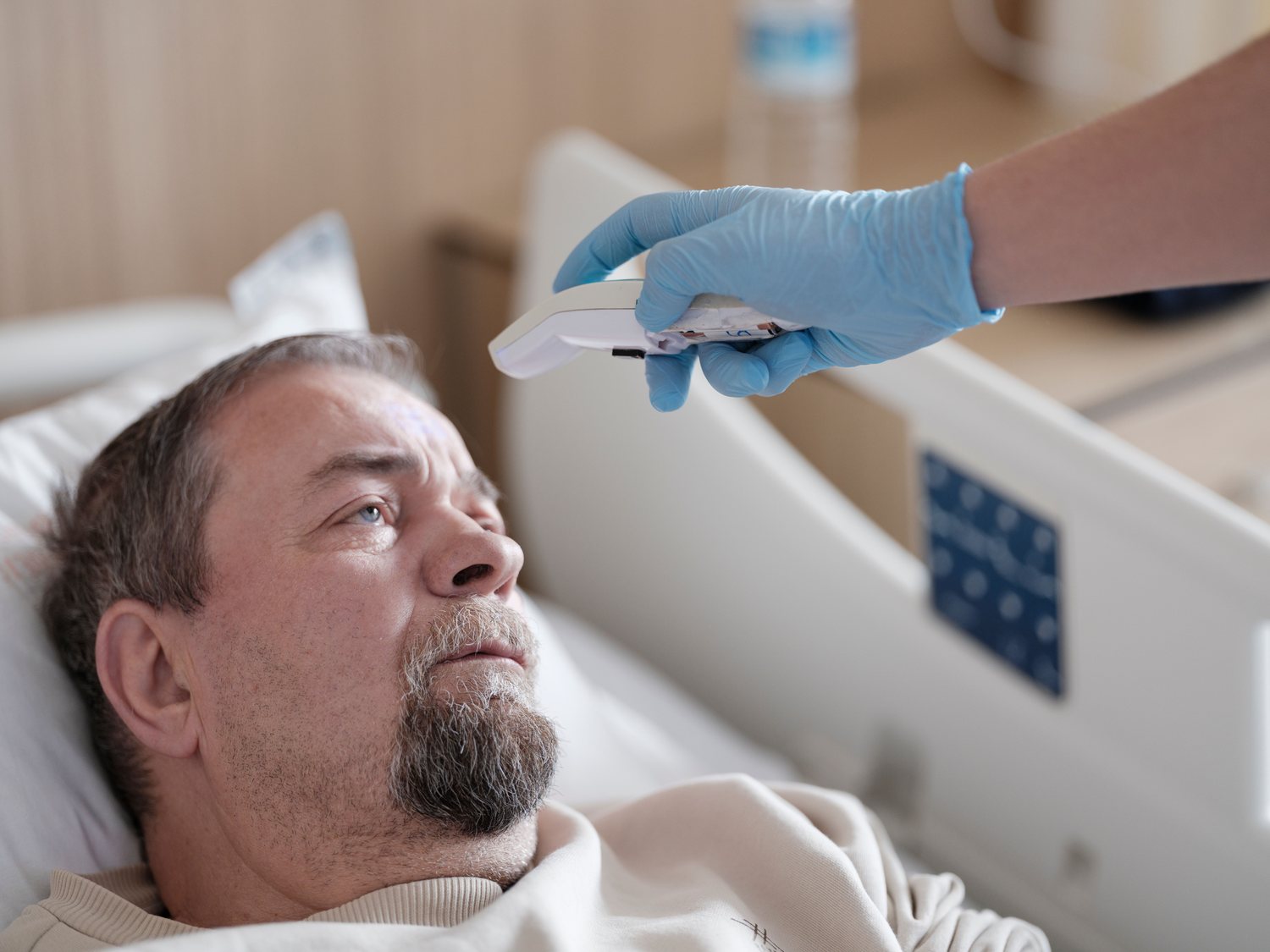 Nurse taking a manual bedside temperature reading, the routine round that continuous monitoring replaces