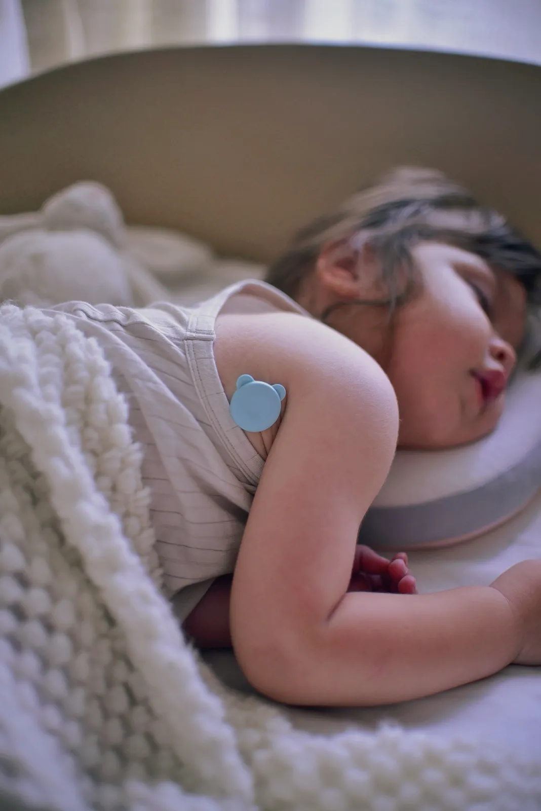 Close-up of the 2g OnCorva sensor attached under a sleeping child's arm with a hypoallergenic patch