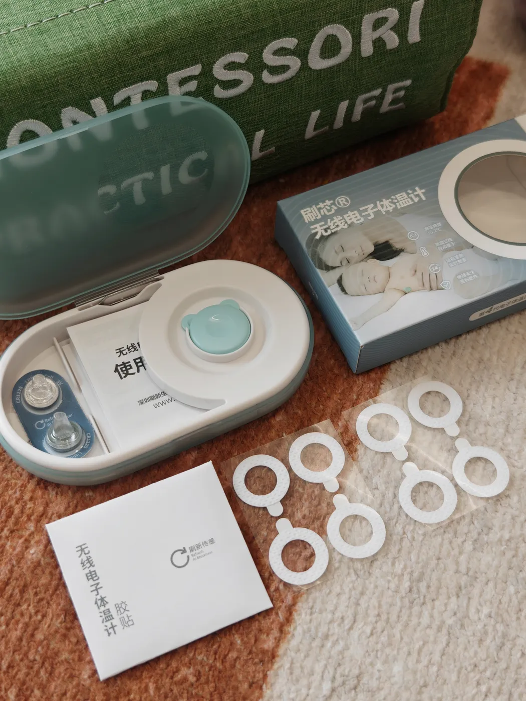 OnCorva wearable thermometer retail kit unboxed — sensor, storage case, hypoallergenic patches, CR1225 battery and manual